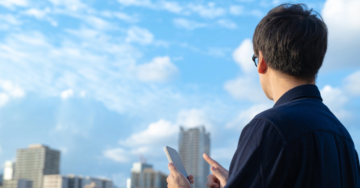 晴天の下スマホを操作している男性の画像