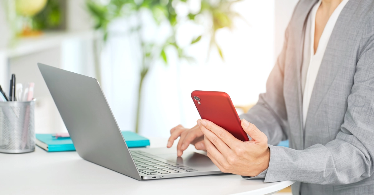 スマホを見ながらPCを操作するビジネスパーソンの画像